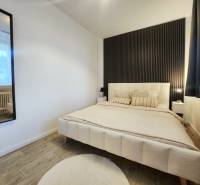 Bedroom in a 2-room apartment with a crib, dark wall, and floor with wood decor.