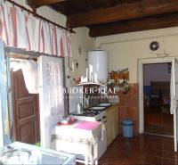 A kitchen in a family house with wooden ceilings, tiles, and curtains.