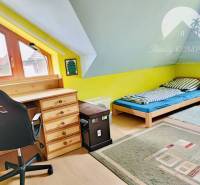Attic room with a desk, bed, and wooden decor flooring in a family house.