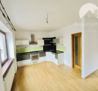 A kitchen in a family house with a wooden decor floor, white cabinets, and green tiles.