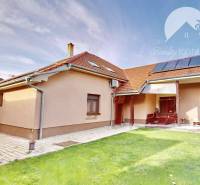 A family house in Komárno surrounded by a green lawn and paving under a blue sky.