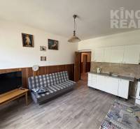 Living room in a family house with a sofa, television, kitchen unit, and wooden decor flooring.