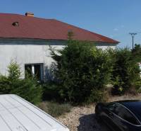 A family house in Zemianska Olča with several parked cars and green bushes in front of it.