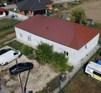 A family house in Zemianska Olča with cars parked on a gravel lot and covered equipment.