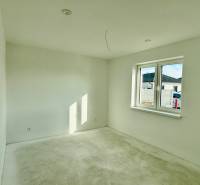 A room in a family house with white walls and a large window, the floor ready for finishing.