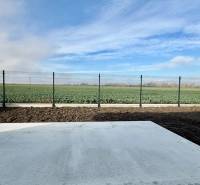 A family house in Topoľnica with a concrete terrace and a view of the field behind the fence.