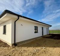 Family house in Topoľnica, simple facade, grassy yard, concrete fence, blue sky.