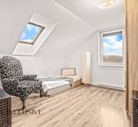Attic room in a family house with an armchair, bed, and wooden decor flooring.