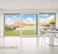 The interior of a family house with a dining nook, glass doors to the garden, and a white floor.