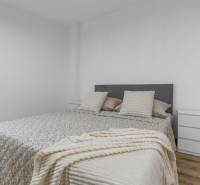 A bright bedroom with a double bed, nightstands, and a wooden decor floor in a three-room apartment.