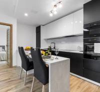 A kitchen in a 3-room apartment with dark cabinets, a dining table, and a wooden decor floor.