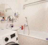 A bathroom in a 3-room apartment with a washing machine, bathtub, and toiletries.