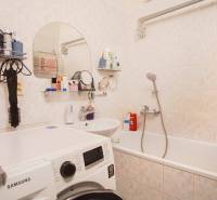 A bathroom in a 3-room apartment with a bathtub and a washing machine, accessories on the shelves.