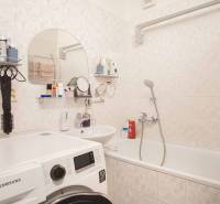 A bathroom of a three-room apartment with a washing machine, a sink, and a bathtub.