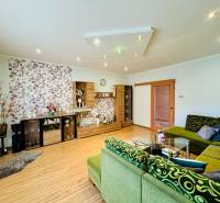 Living room with a sofa, wood-patterned flooring, and patterned wallpaper in a family house.