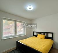 A bright bedroom with a bed, a yellow bedspread, and three windows in a family house.