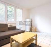 Living area of a studio apartment with a sofa, table, and refrigerator.