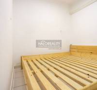 A bedroom in a one-room apartment with a wooden bed and white walls.