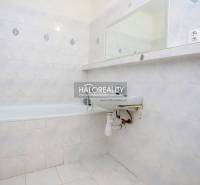 Bathroom in a one-room apartment with a bathtub, sink, and tiled cladding.