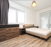A bedroom in a three-room apartment with a wooden decor floor, a bed, and a dresser.