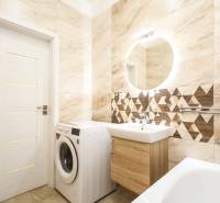 A bathroom in a 3-room apartment with a washing machine, a bathtub, and geometric tiles.