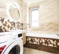 A bathroom in a three-room apartment with geometric tiles and a washing machine next to the bathtub.