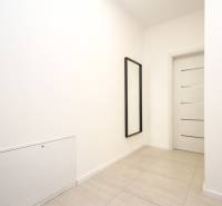 A hallway in a 3-room apartment with white walls, a mirror, and lightly decorated tiles.