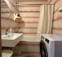 A bathroom with a washing machine, bathtub, and sink in a 3-room apartment, tiled with a pink pattern.