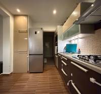A kitchen in a 3-room apartment with a gas stove, refrigerator, and wooden decor flooring.