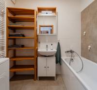 A bathroom in a 2-room apartment with a bathtub, a washbasin cabinet, and wooden shelves.