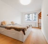 A bright bedroom with a bed, two pillows, and a shelf in a 2-room apartment, with a wooden-patterned floor.