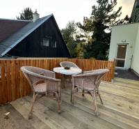 A terrace with rattan seating and wooden decor, surrounded by greenery.
