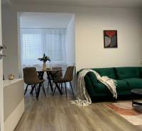 Living room of a 3-room apartment with a green sofa, table, chairs, and a wooden-patterned floor.