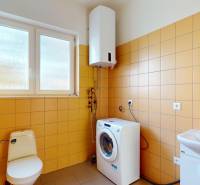 A bathroom with a washing machine, toilet, and sink, tiled with yellow tiles.