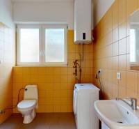A bathroom with a sink, toilet, and washing machine, covered in orange tiles.