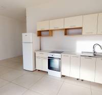 Kitchen unit, stove, and refrigerator on white tiles in commercial premises.