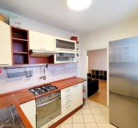 A kitchen in a 3-room apartment with a gas stove, stainless steel refrigerator, and wooden decor flooring.