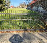A metal gate surrounded by pillars and greenery in Veľké Ludince on Park Street and the main road.