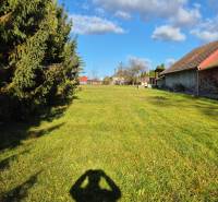 A grassy area with wooden shelters and trees in the park and main road in Veľké Ludince.