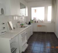 Offices with a kitchenette in white color, tiles, sink, windows with flowers, and radiator.