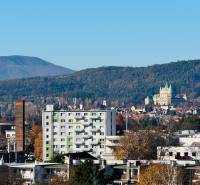 View of Prievidza from I. Krasko Street with nearby buildings and green hills.