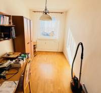 A room in a 4-room apartment with a wooden decor floor, a desk, and shelves.