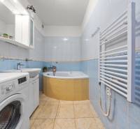A bathroom in a 2-room apartment with a corner bathtub, a washing machine, and light blue tiles.