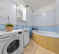 A bathroom with a bathtub, a washing machine, and light tiles in a 2-room apartment.