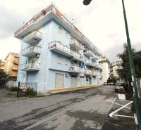 Building on Minzoni Street in Scalea with multi-story balconies and parking lot.