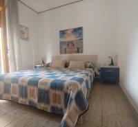 A bedroom in a two-room apartment with a double bed, pictures on the walls, and blue nightstands.