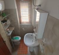 A bathroom in a 2-room apartment with a sink, toilet, and storage shelf.