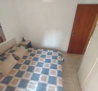 Bedroom in a two-room apartment with a double bed, nightstand, and a picture on the white wall.