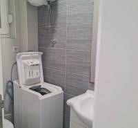 Bathroom with a washing machine and a sink in a 3-room apartment, light gray tiles.
