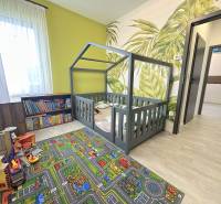 Children's room with a house-shaped bed, patterned carpet, bookshelf, and plant wallpaper in a family house.